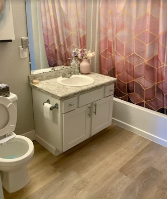 A bathroom featuring a white vanity with a granite countertop, a toilet, and a pink geometric shower curtain.