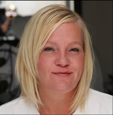 Close-up portrait of a person with blonde hair parted to the side, looking at the camera with a neutral expression.
