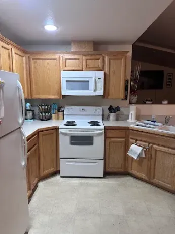 A kitchen with wood cabinets, white appliances including a stove and over-the-range microwave, and light-colored flooring.