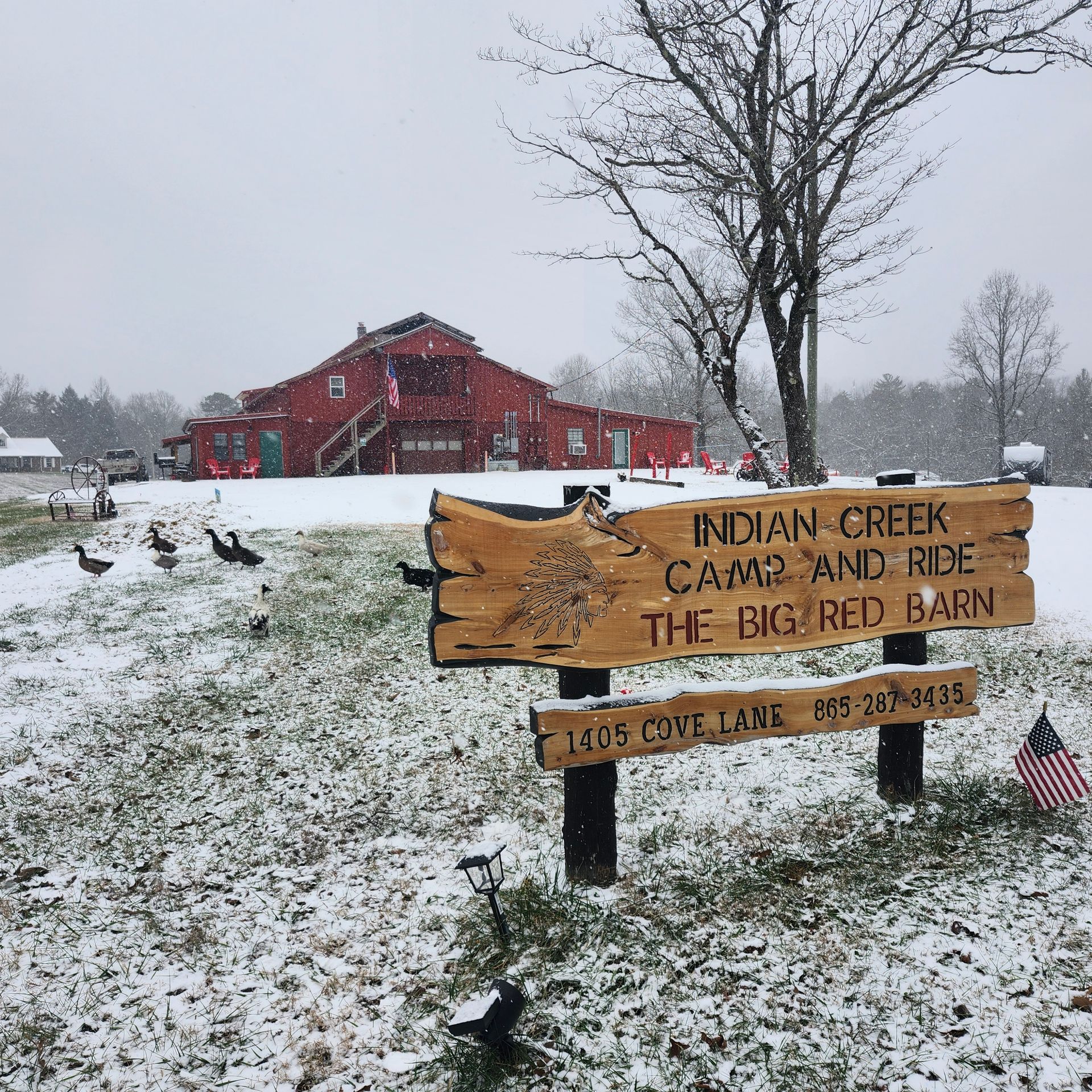 Snowy roadside sign for Indian Creek Camp and Ride in front of a red barn-like building
