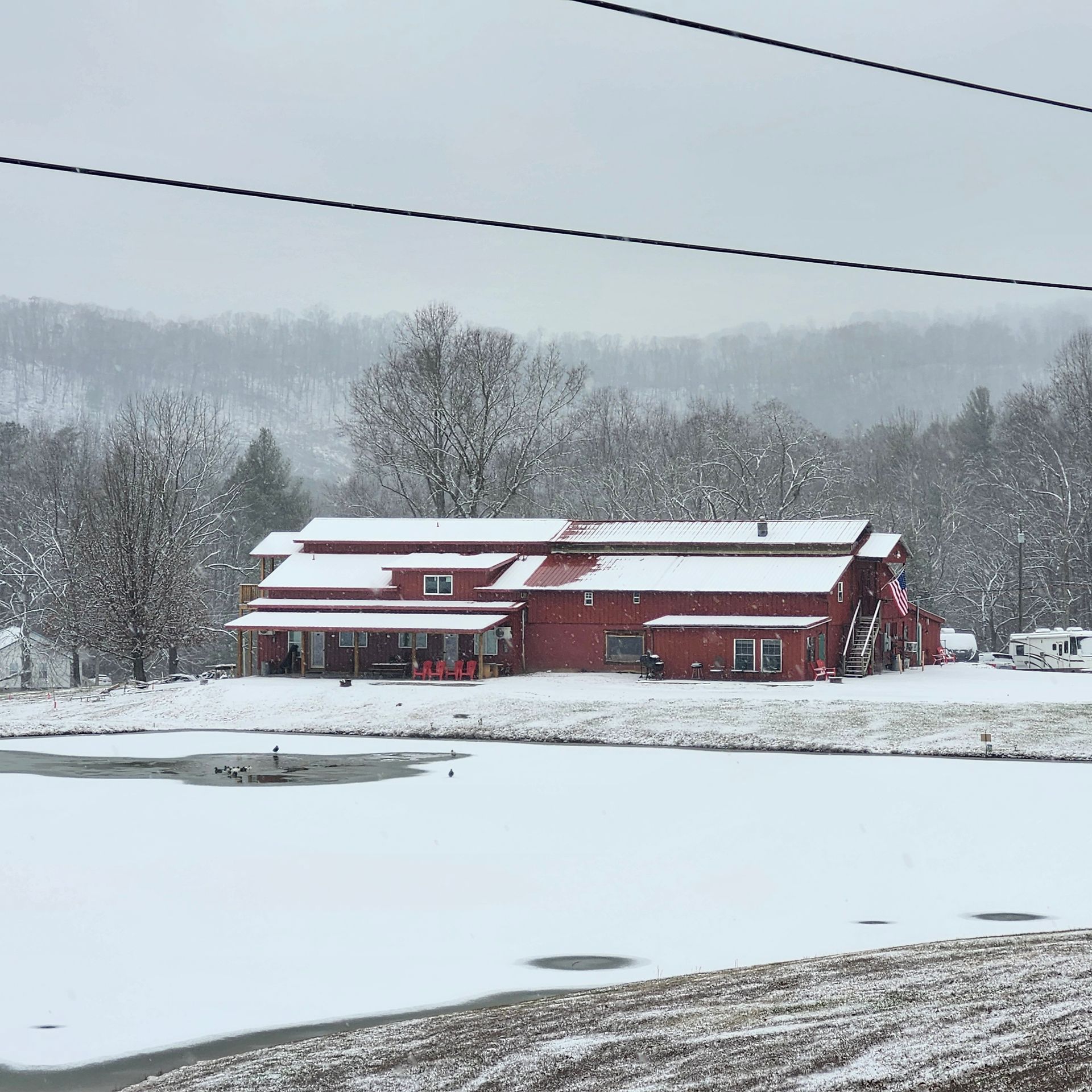 Red barn-like house beside a frozen pond in a snowy rural landscape