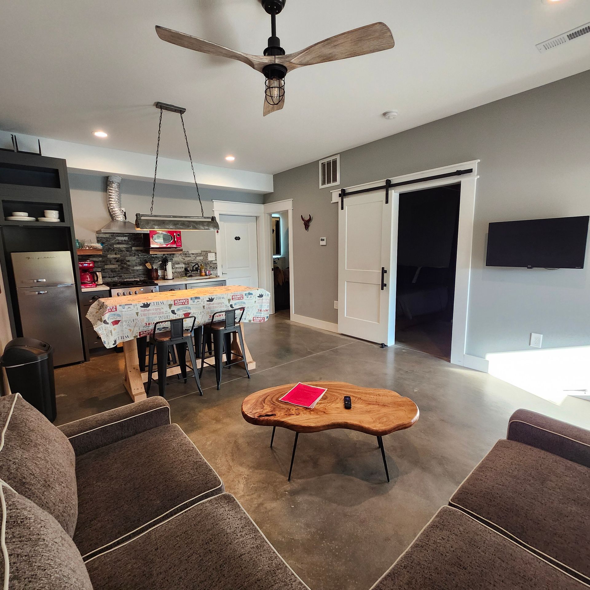Modern living room with sectional sofa, coffee table, kitchen island, ceiling fan, and wall-mounted TV