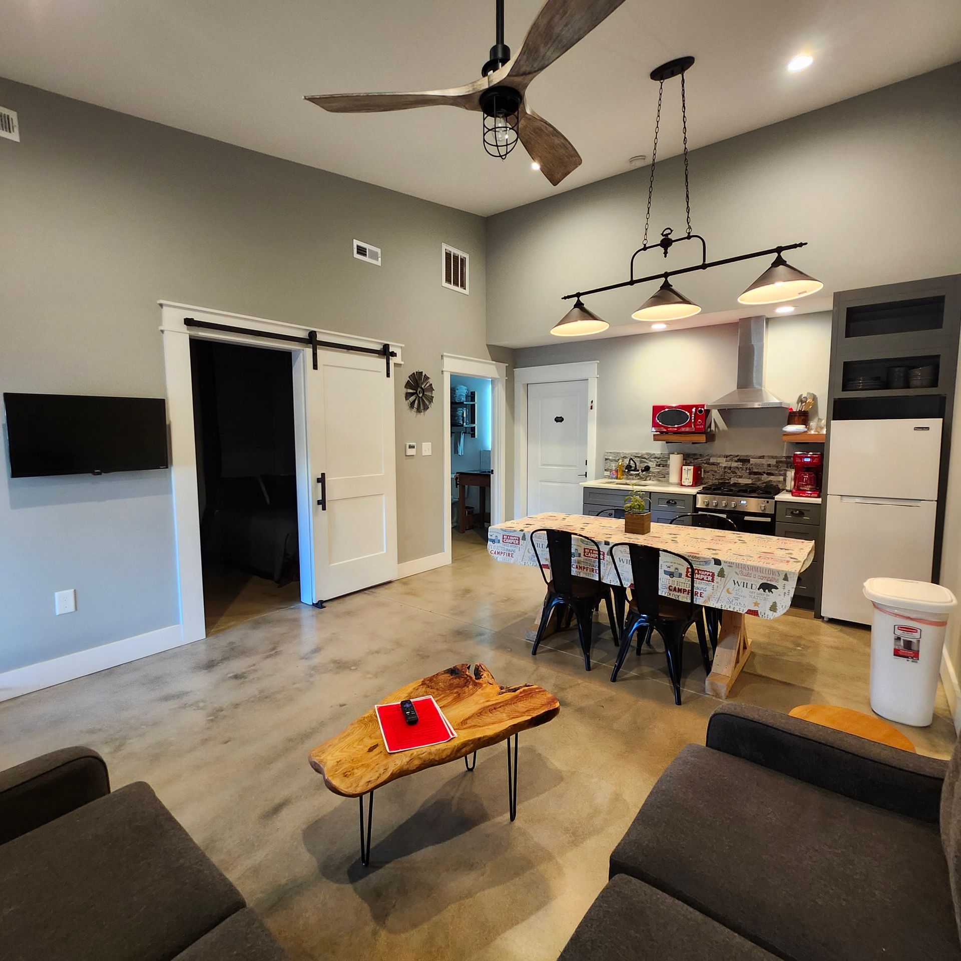 Modern open-concept living room and kitchen with sofa, coffee table, ceiling fan, and pendant lights