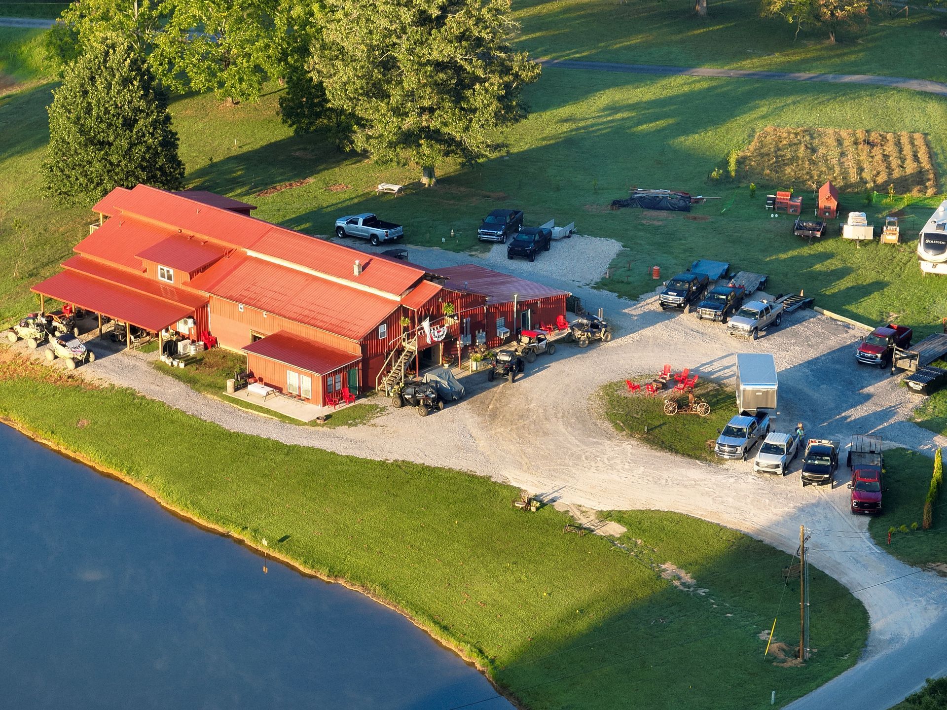 Aerial view of a red-roofed lakeside building with parked cars and a gravel lot beside the water