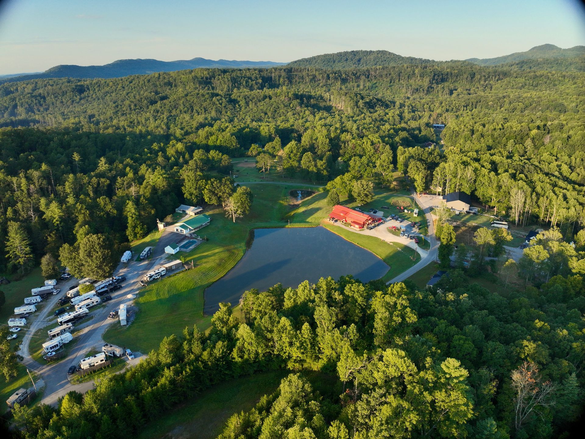 Aerial view of a forested lakeside campground with tents, cabins, and a small dock by the water
