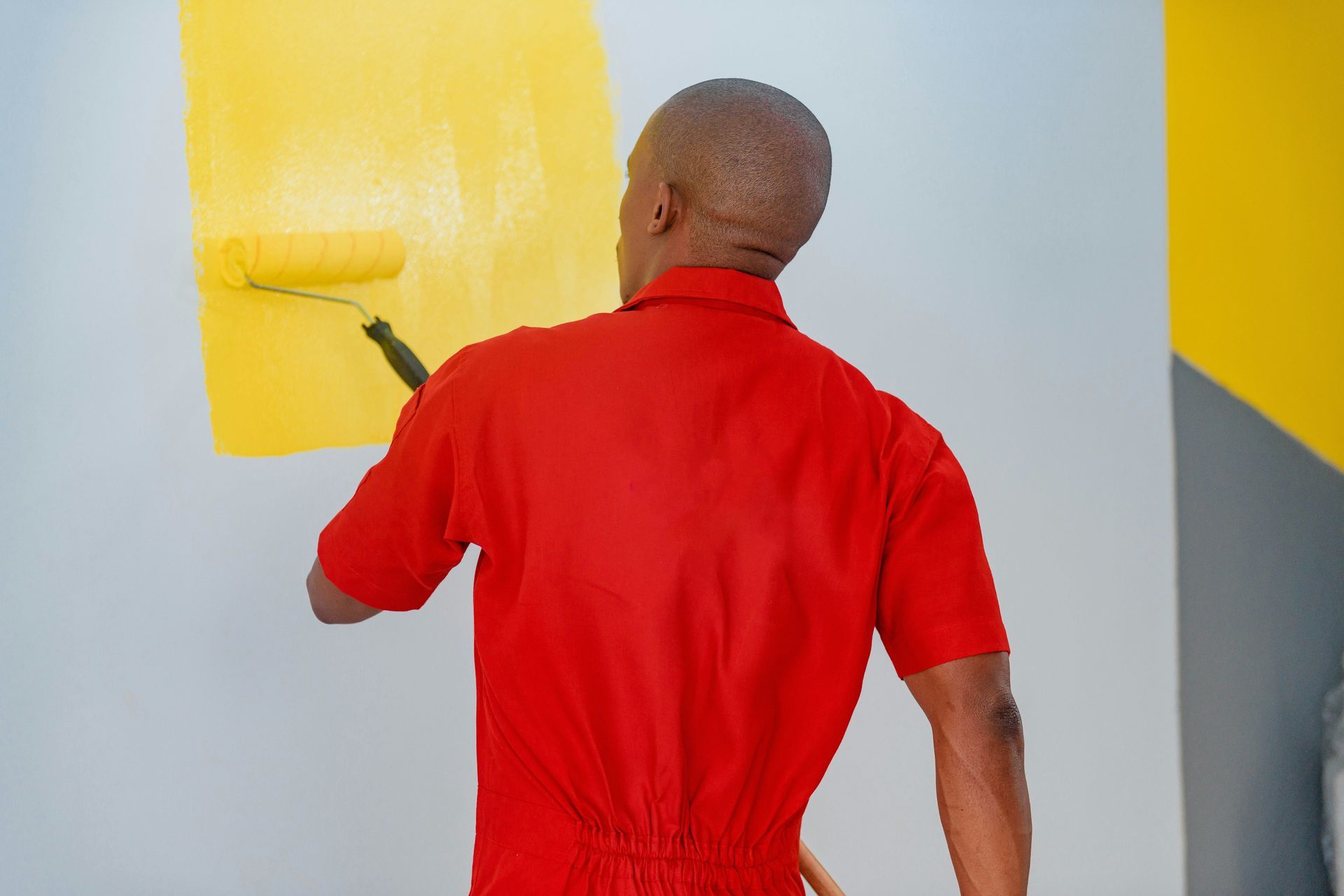 Person in a red shirt painting a white wall with yellow paint.