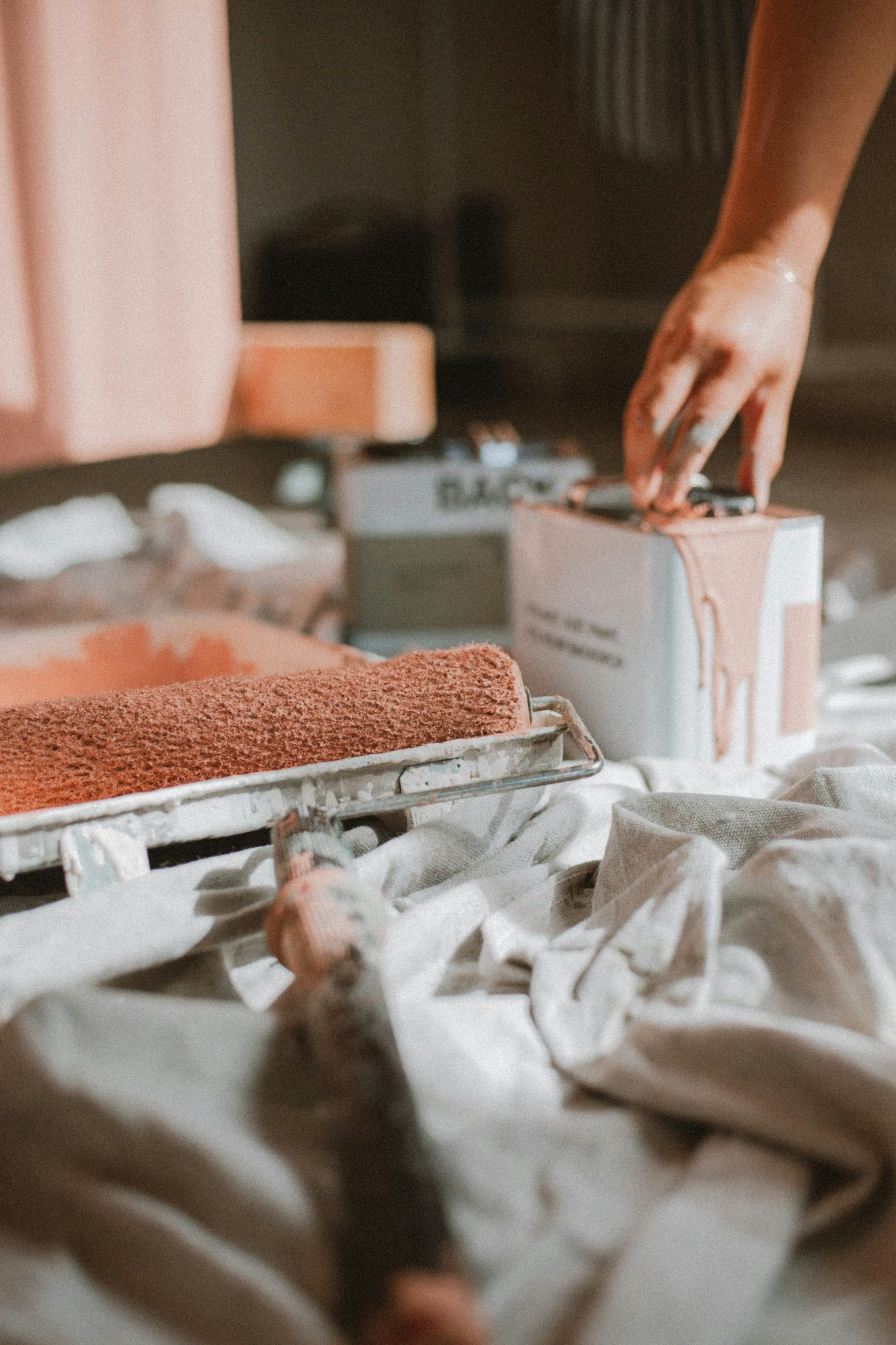 Hand placing a boxed item on a bed beside a tray of coffee beans and wrapping paper