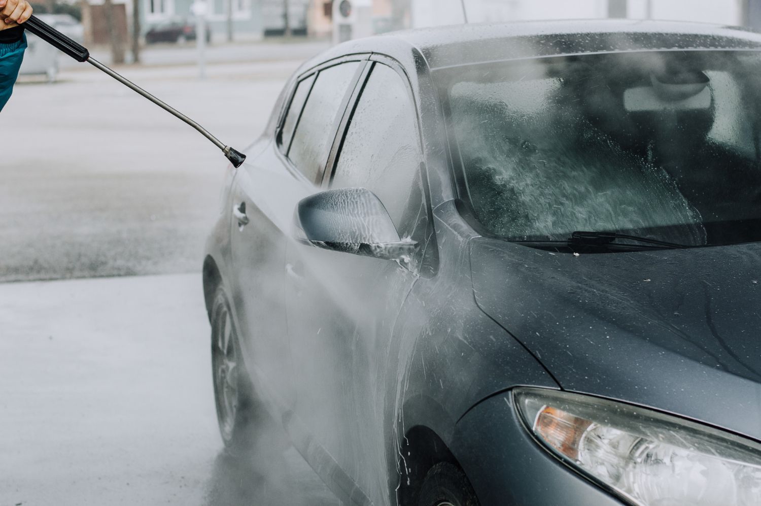 A person is washing a car with a high pressure washer.
