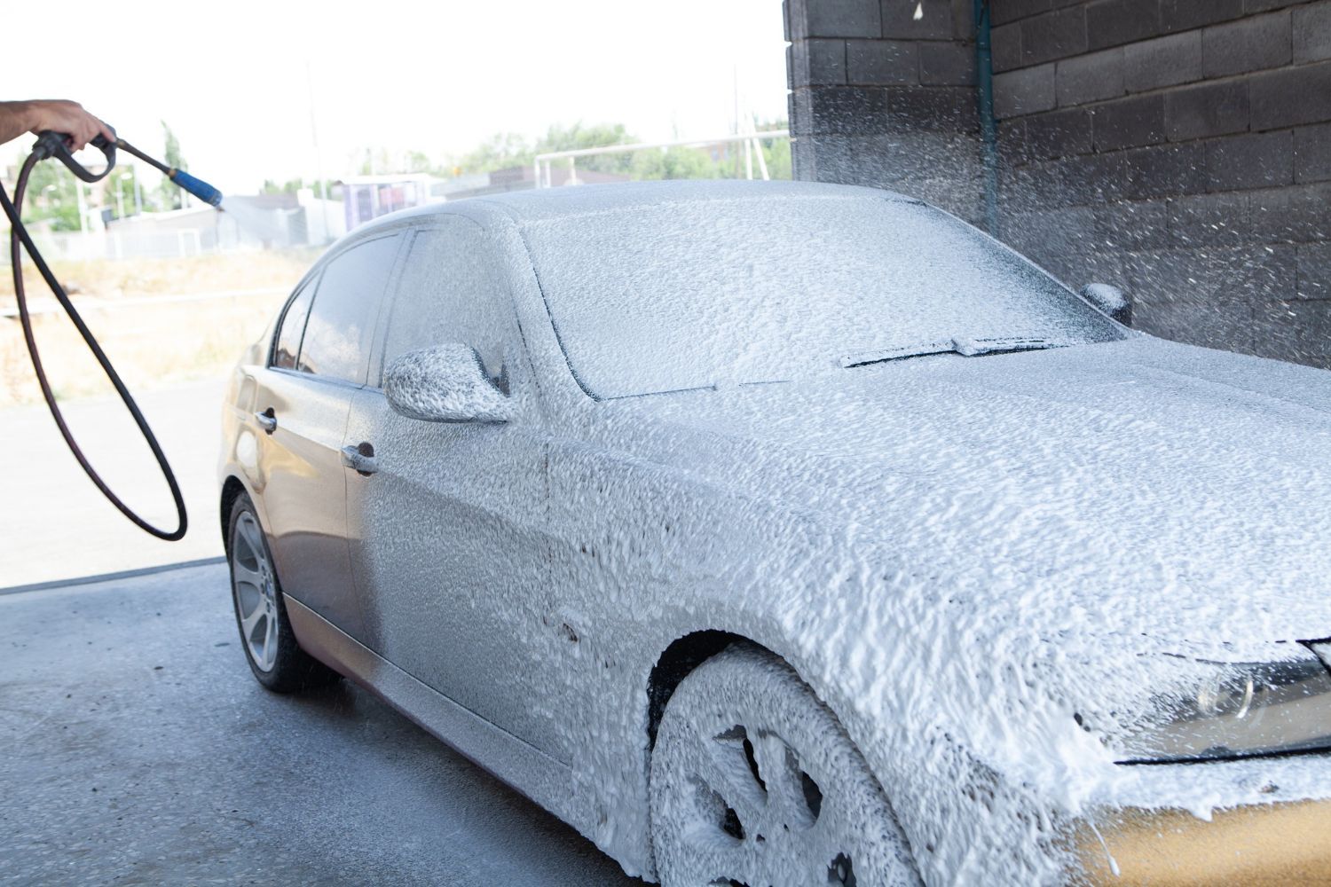 A black car is covered in foam at a car wash.