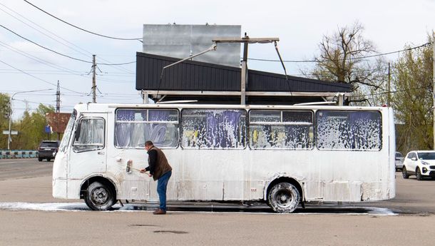 A man is washing a white bus in a parking lot.
