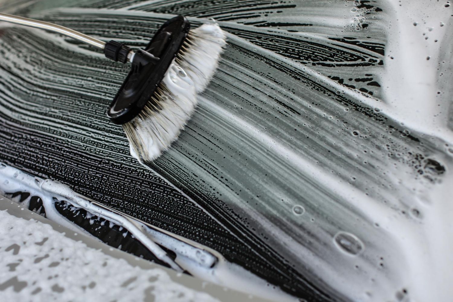 A person is washing a car with a brush and soap.
