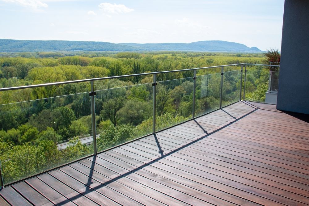 A wooden deck with a glass railing overlooking a forest.