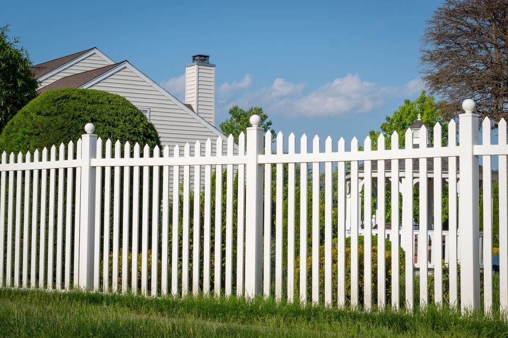 A white picket fence surrounds a lush green yard in front of a house.