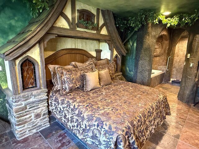 Cozy rustic bedroom with stone fireplace, wooden bed frame, and floral bedding under leafy canopy