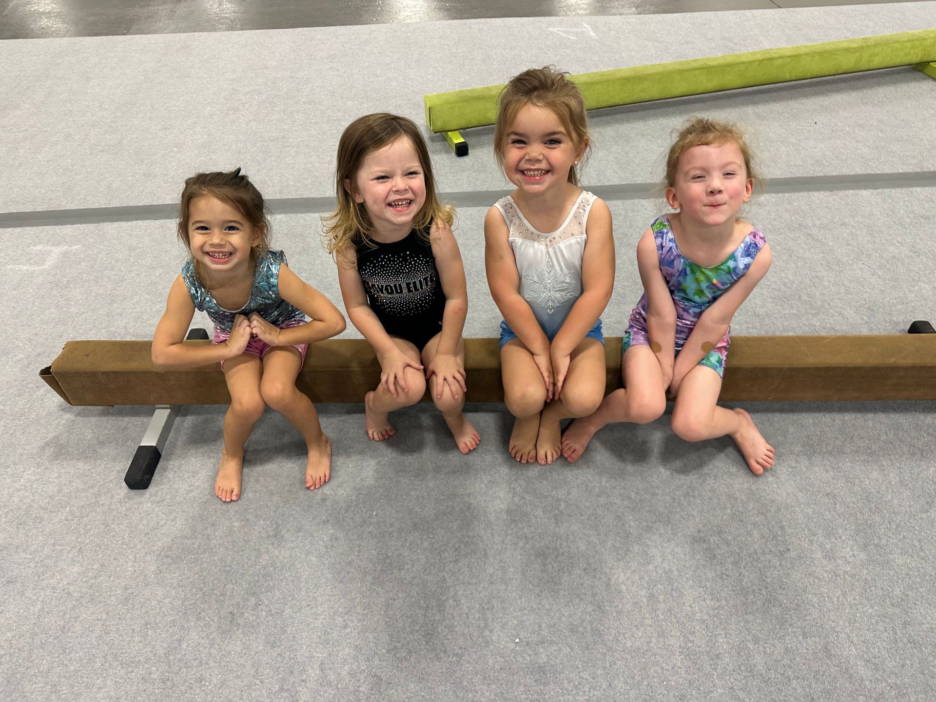 A young child, assisted by an adult, does a forward roll on a blue and red mat in a gym.