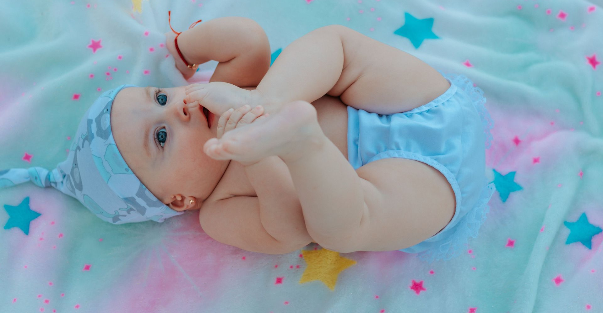 A woman in yellow lies on her back, holding a laughing baby in the air during an exercise class.