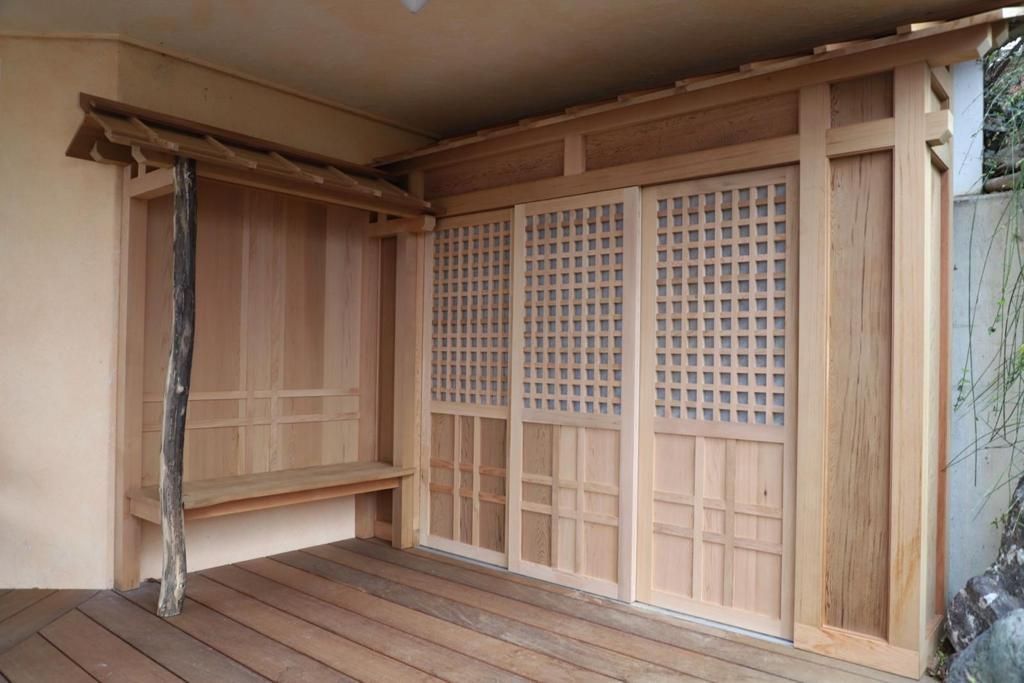 Een houten gebouwtje met schuifdeuren en een bankje.