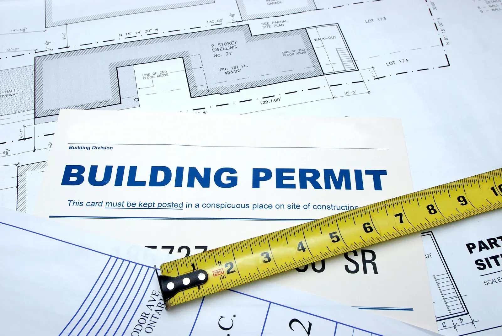 A yellow tape measure sits on top of a building permit