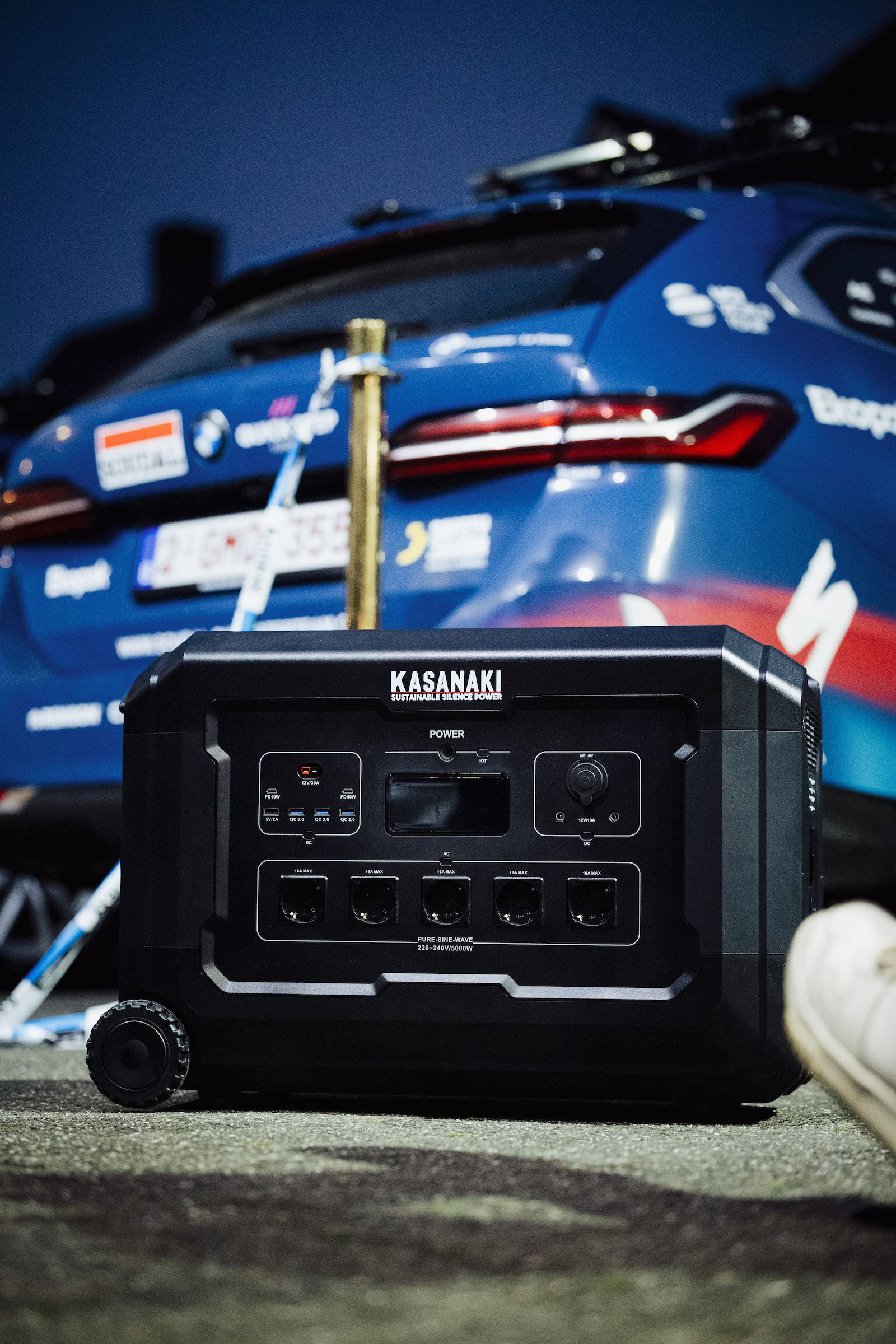 Black generator in front of a blue race car in a garage or pit area