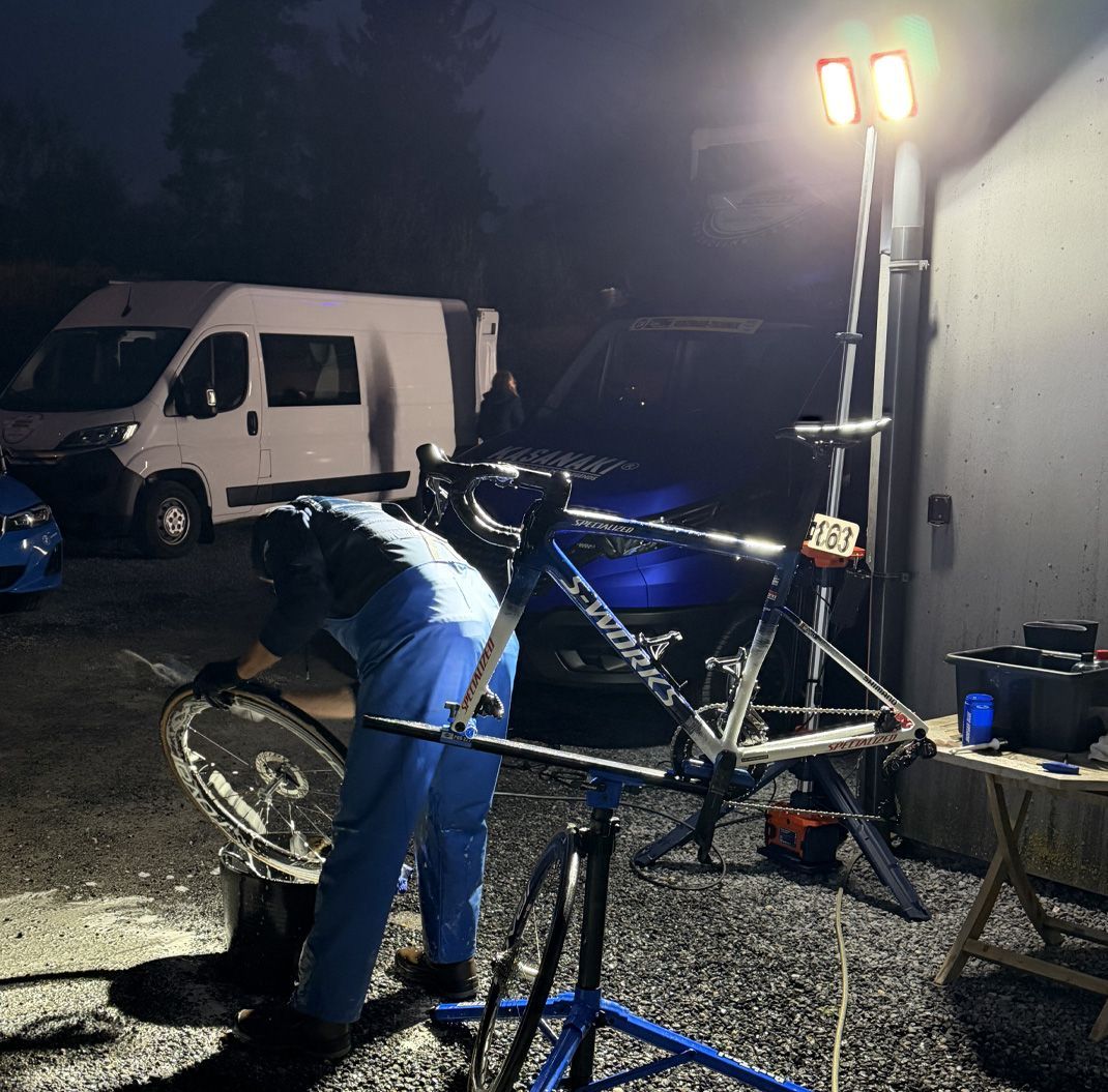 Person working on a bicycle under bright lights in a dark outdoor garage or driveway.