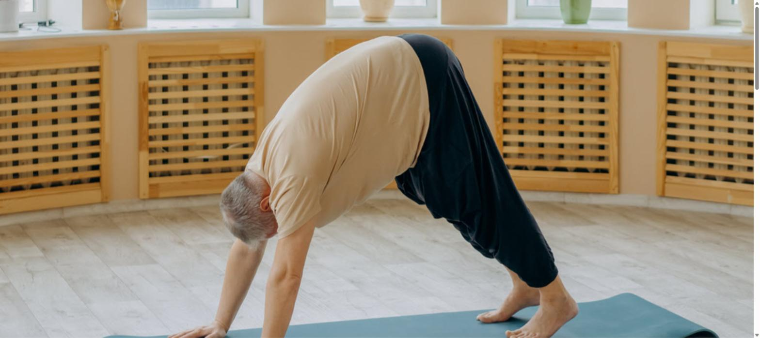 Older adult with gray hair doing a downward dog yoga pose on a teal mat
