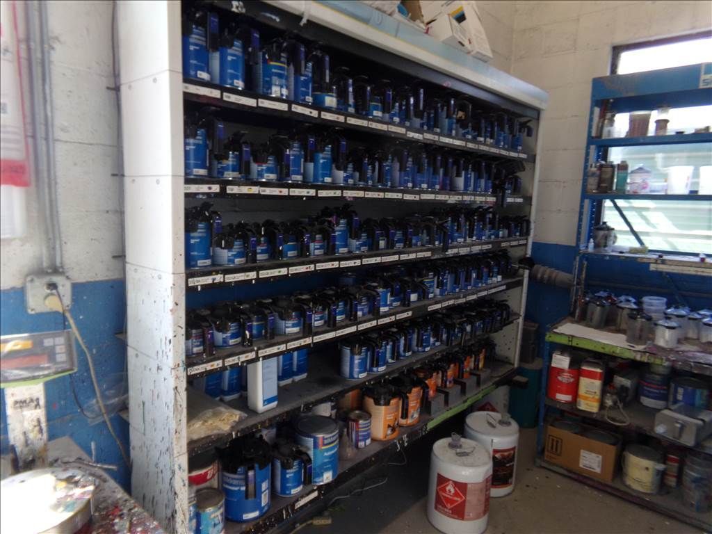 Shelves packed with various paint cans in a workshop setting, primarily blue and orange.