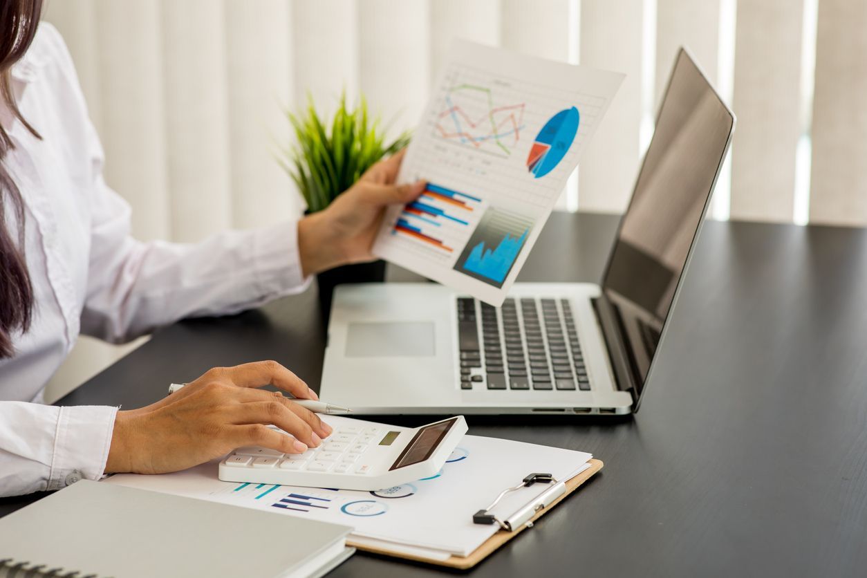 A woman is sitting at a desk with a laptop and a calculator.