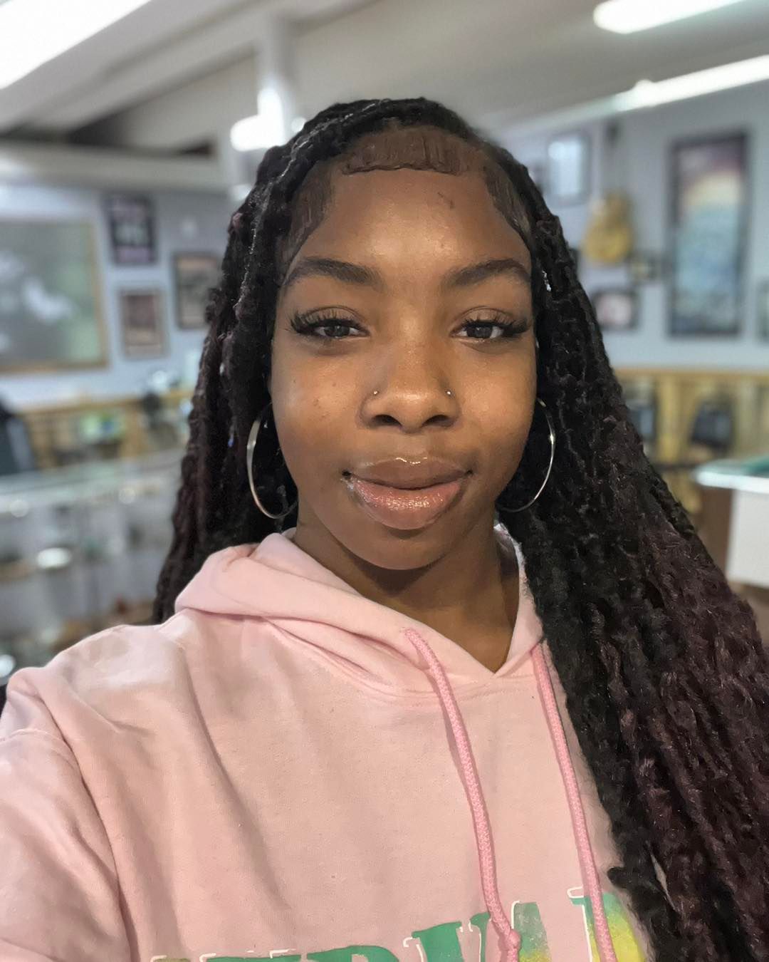 Woman with braided hair, wearing a pink hoodie, and silver hoop earrings, in a room with displays.