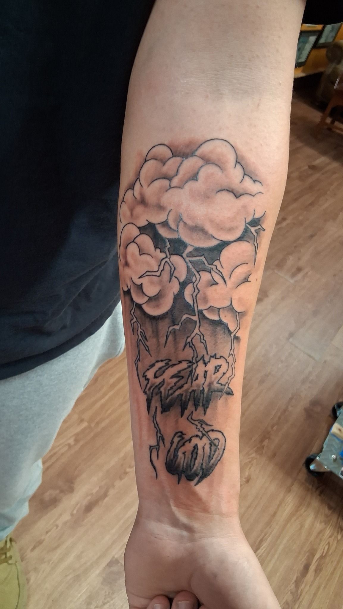 Forearm tattoo of grey clouds and a skull shape with a dark, shaded background.