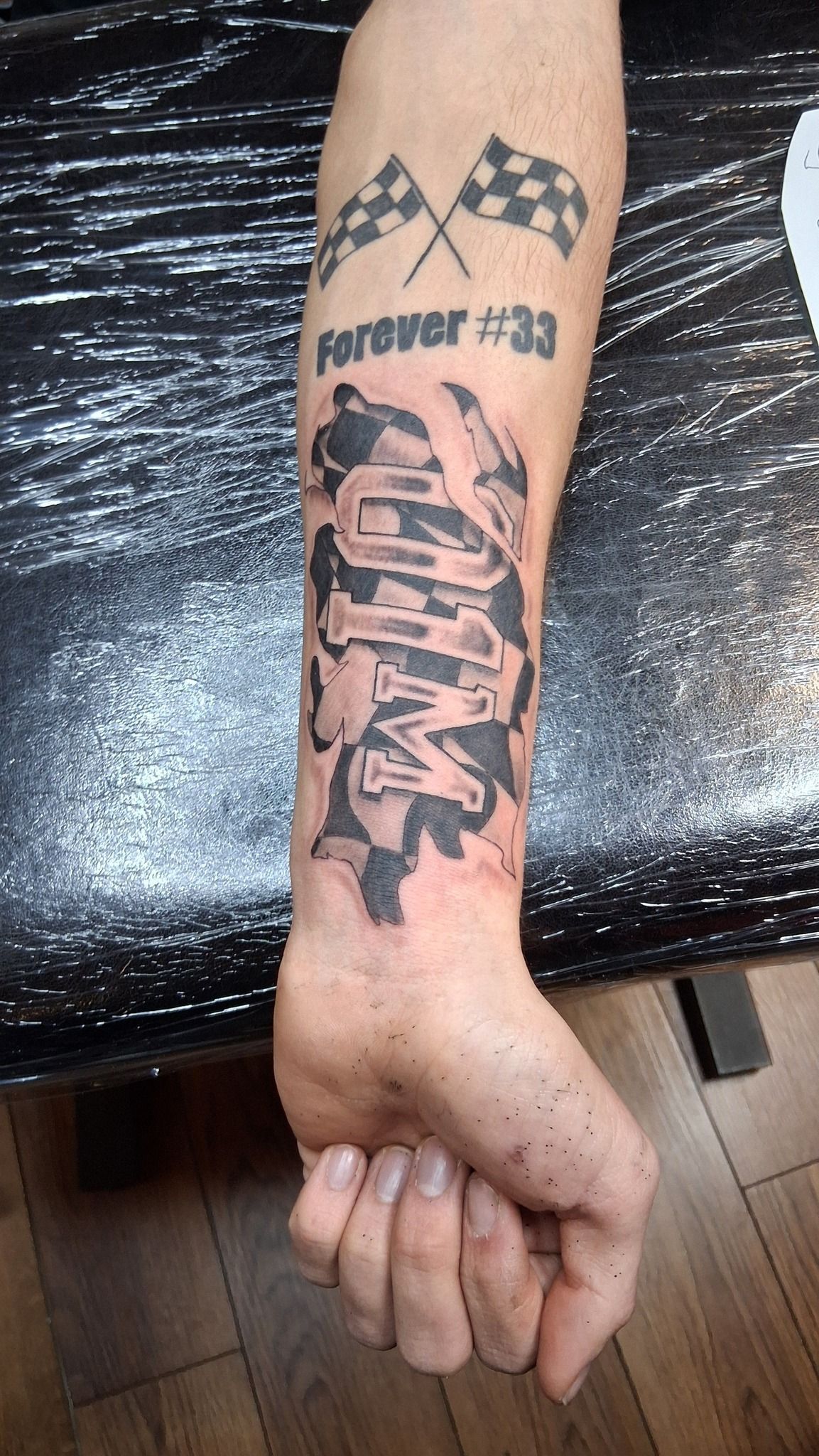 Tattoo of two skulls with smoky swirls on a person's forearm. One skull has clasped skeletal hands in prayer.