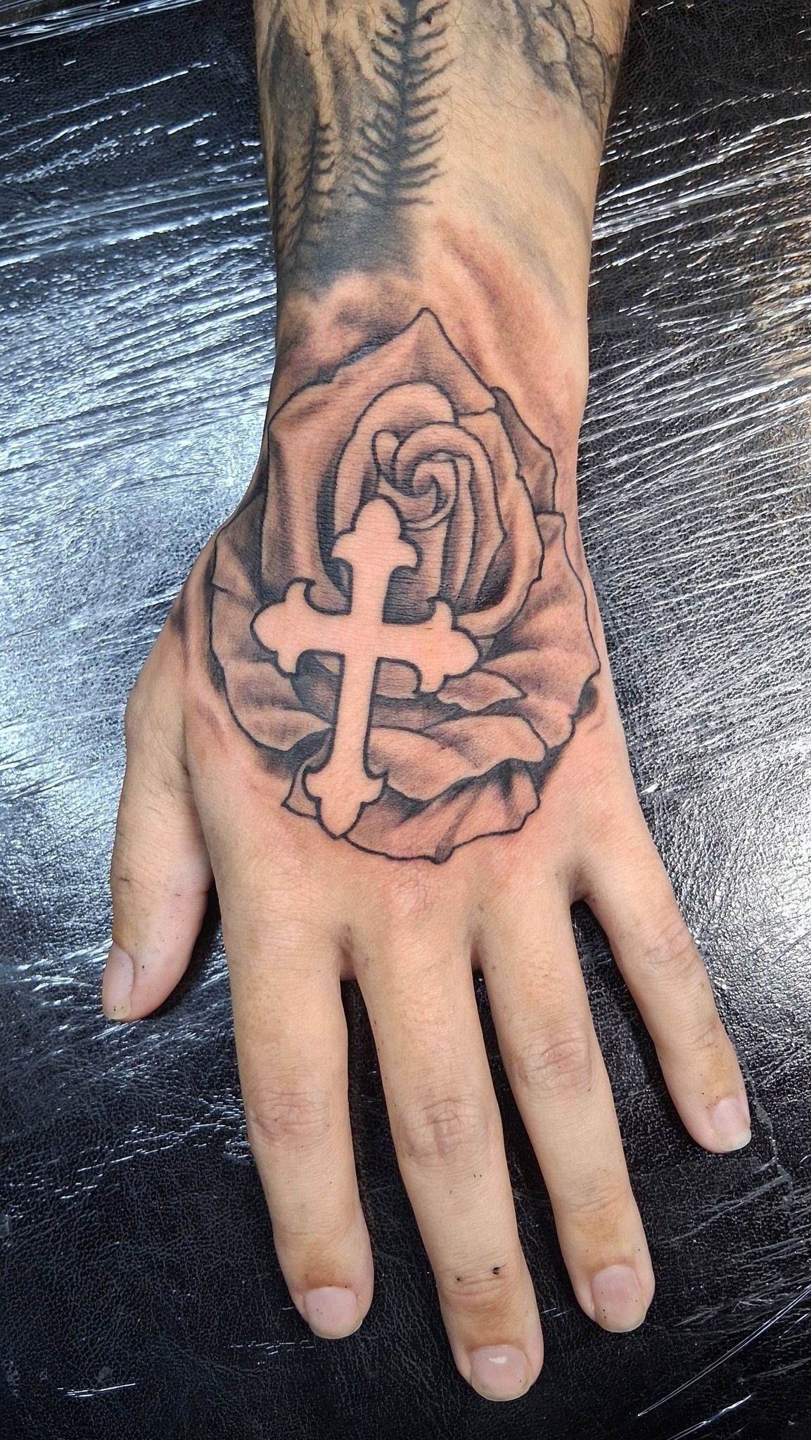 Hand tattoo: Cross inside a rose.