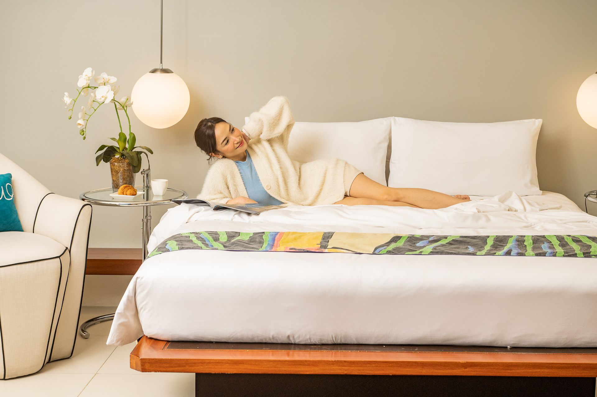 Person relaxing on a white bed in a bright, modern bedroom
