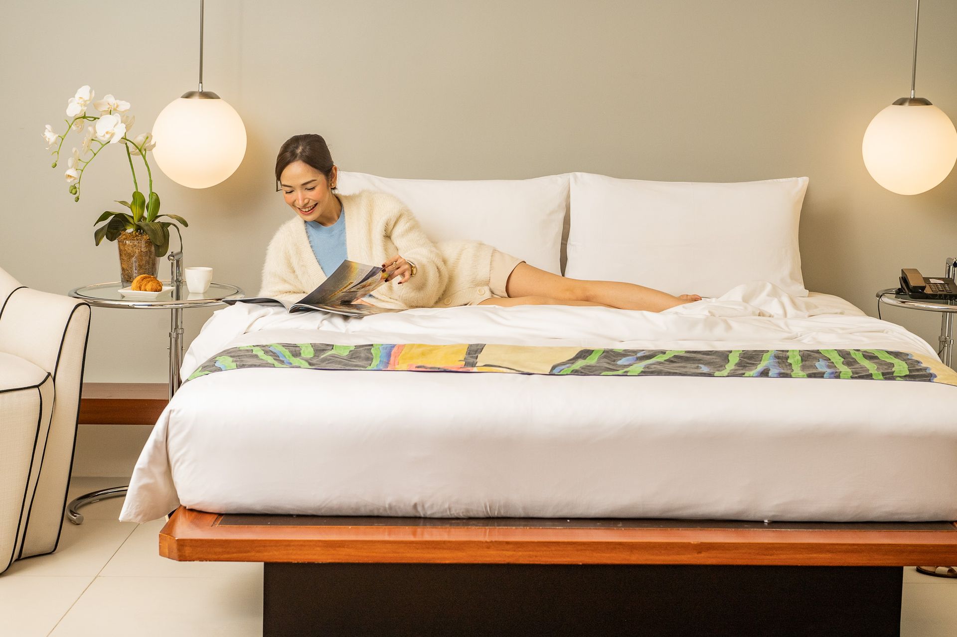 Woman reading to a cat on a bed in a bright bedroom with hanging globe lights