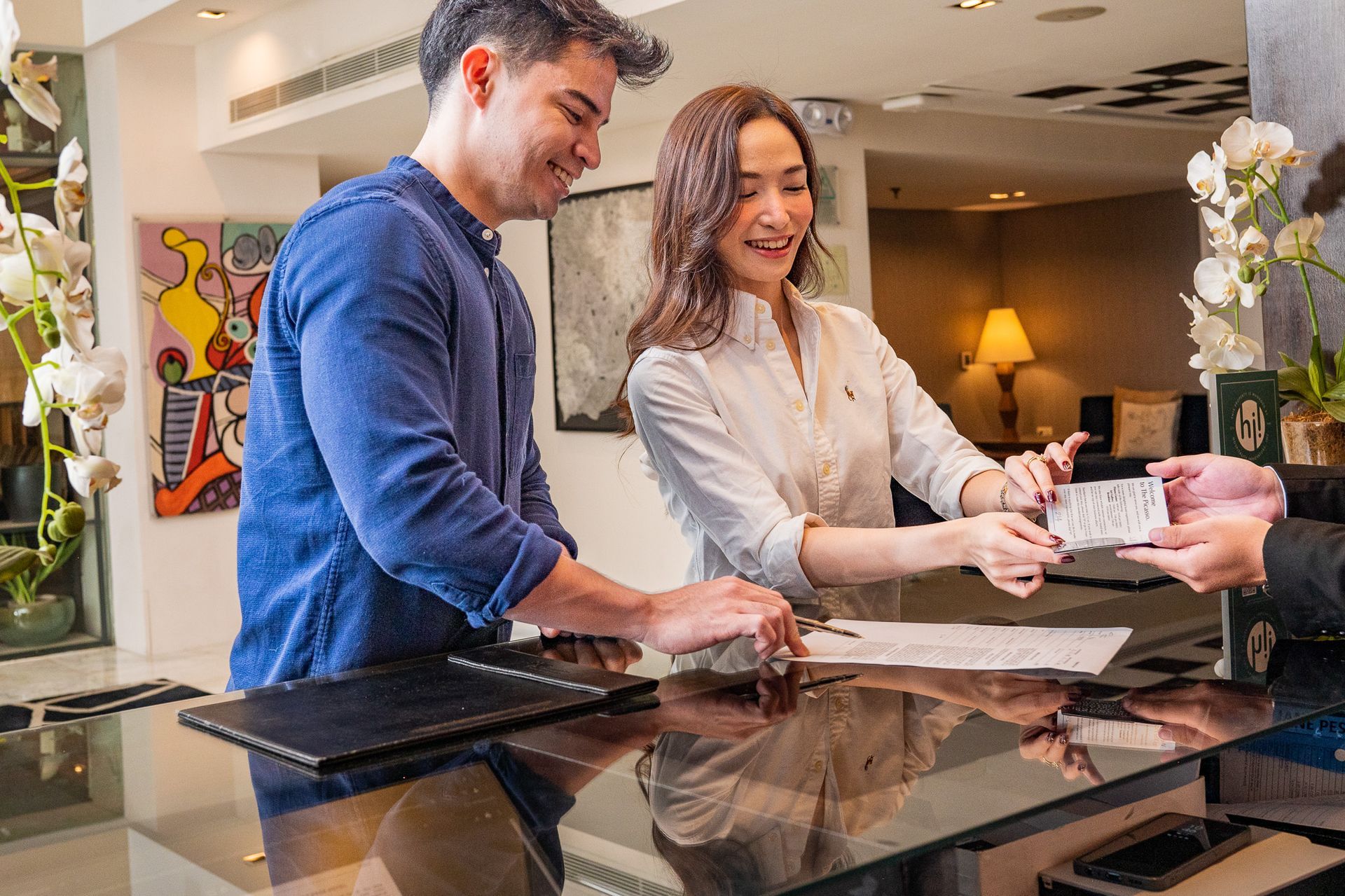 Couple checking in at a hotel front desk; handing papers to a receptionist.