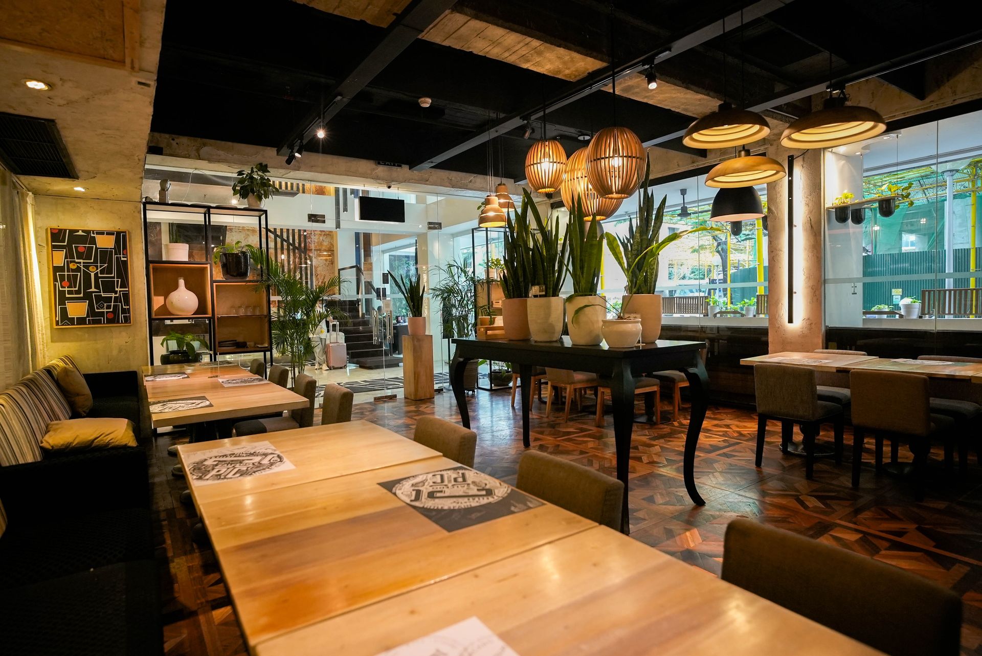 Restaurant interior with wooden tables, decorative plants, and pendant lights.