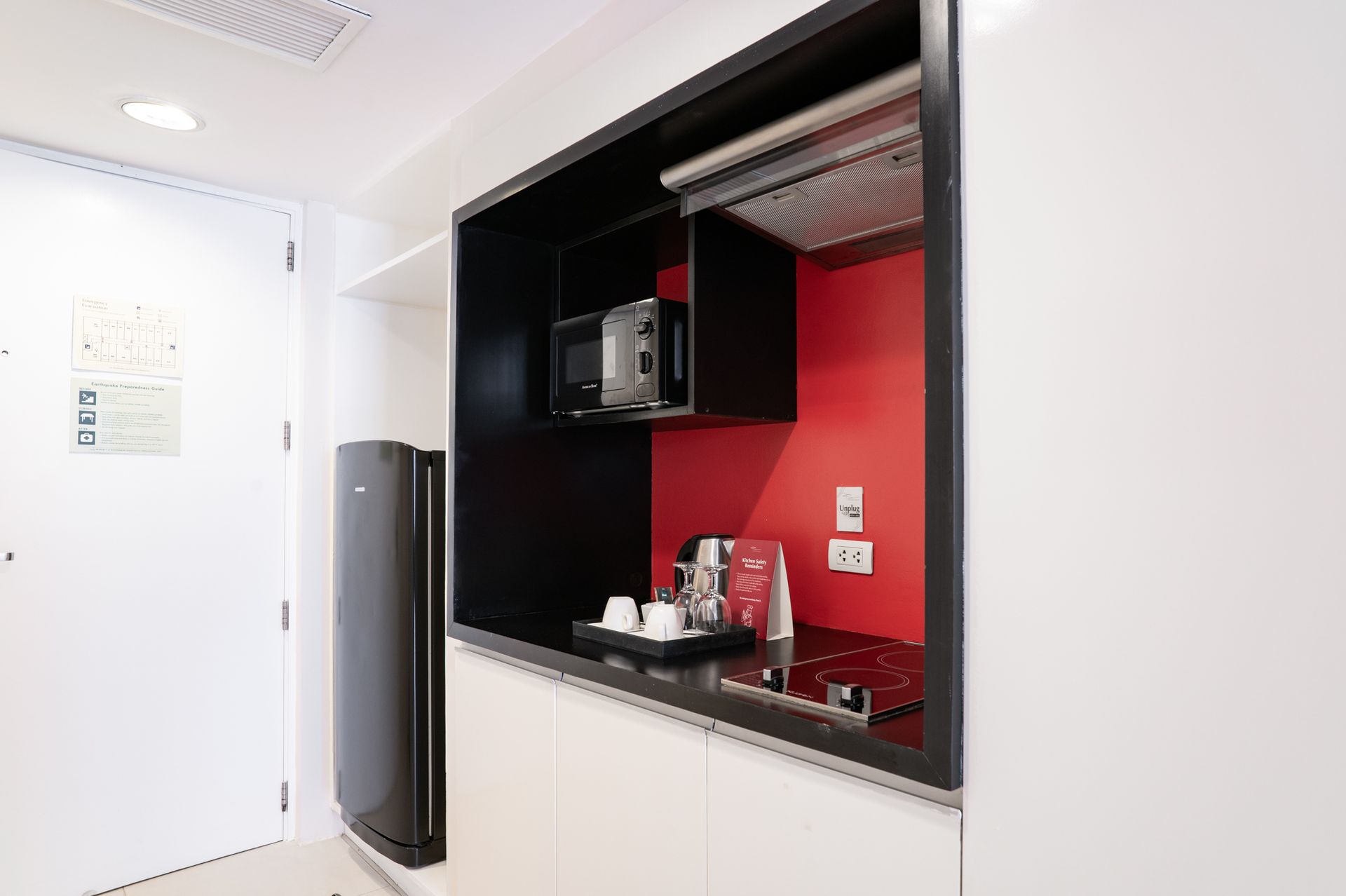 Modern kitchenette nook with black shelving, red back panel, microwave, and small sink area