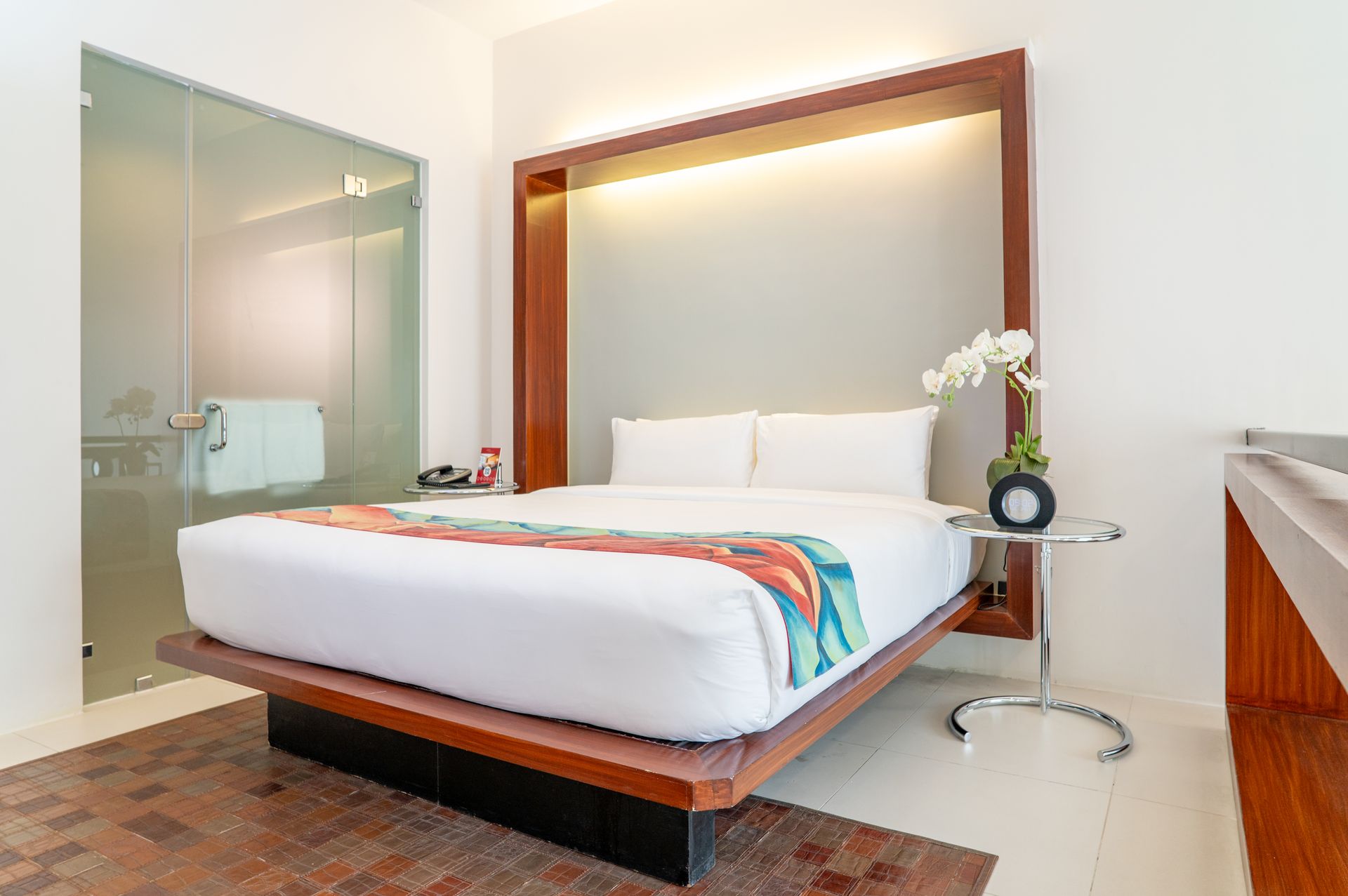 Modern bedroom with a white bed, wood-framed headboard, glass shower, and small side table with flowers