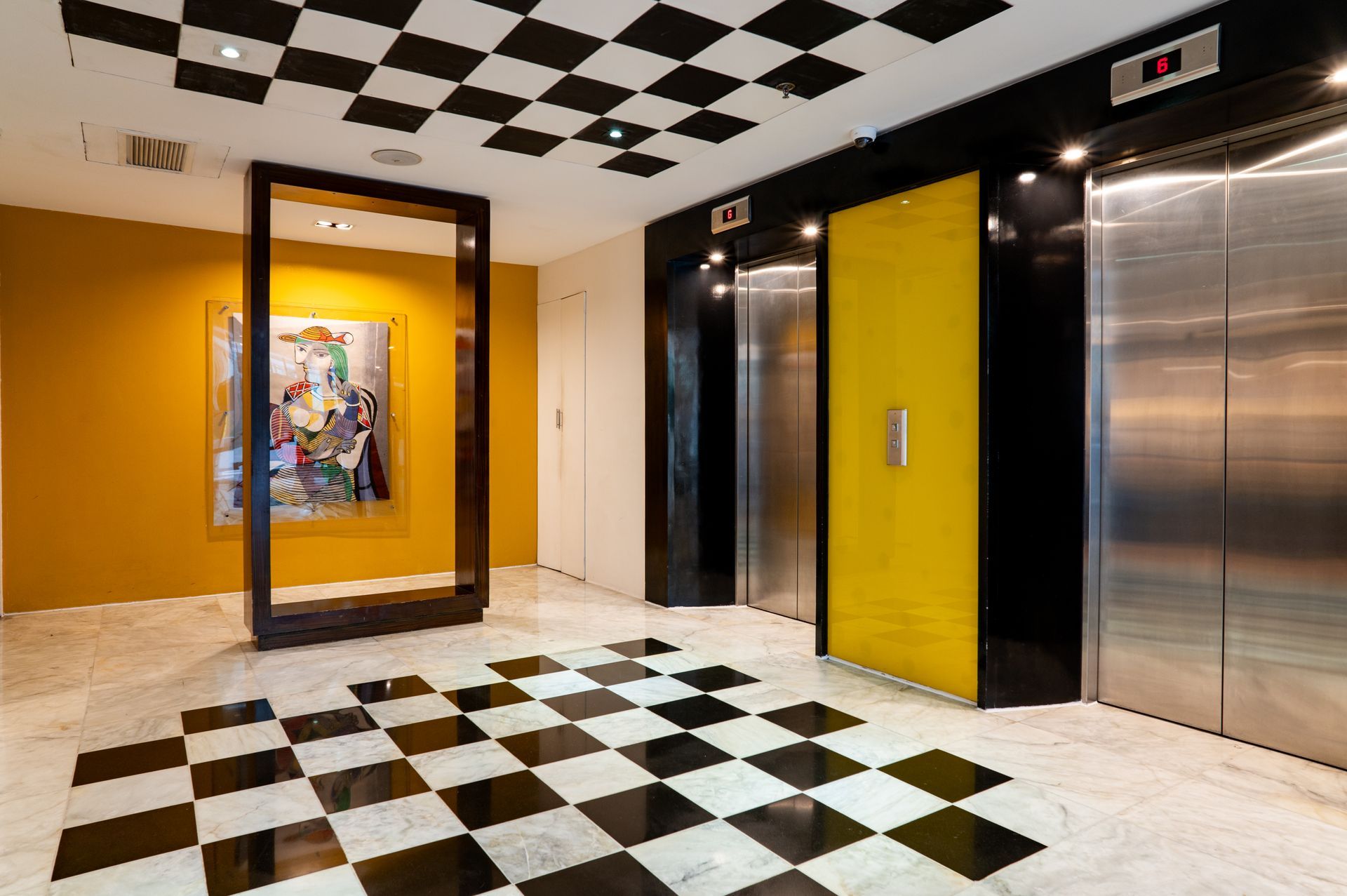 Modern lobby with black-and-white checkerboard floor and ceiling, colorful elevator doors, and red wall panels