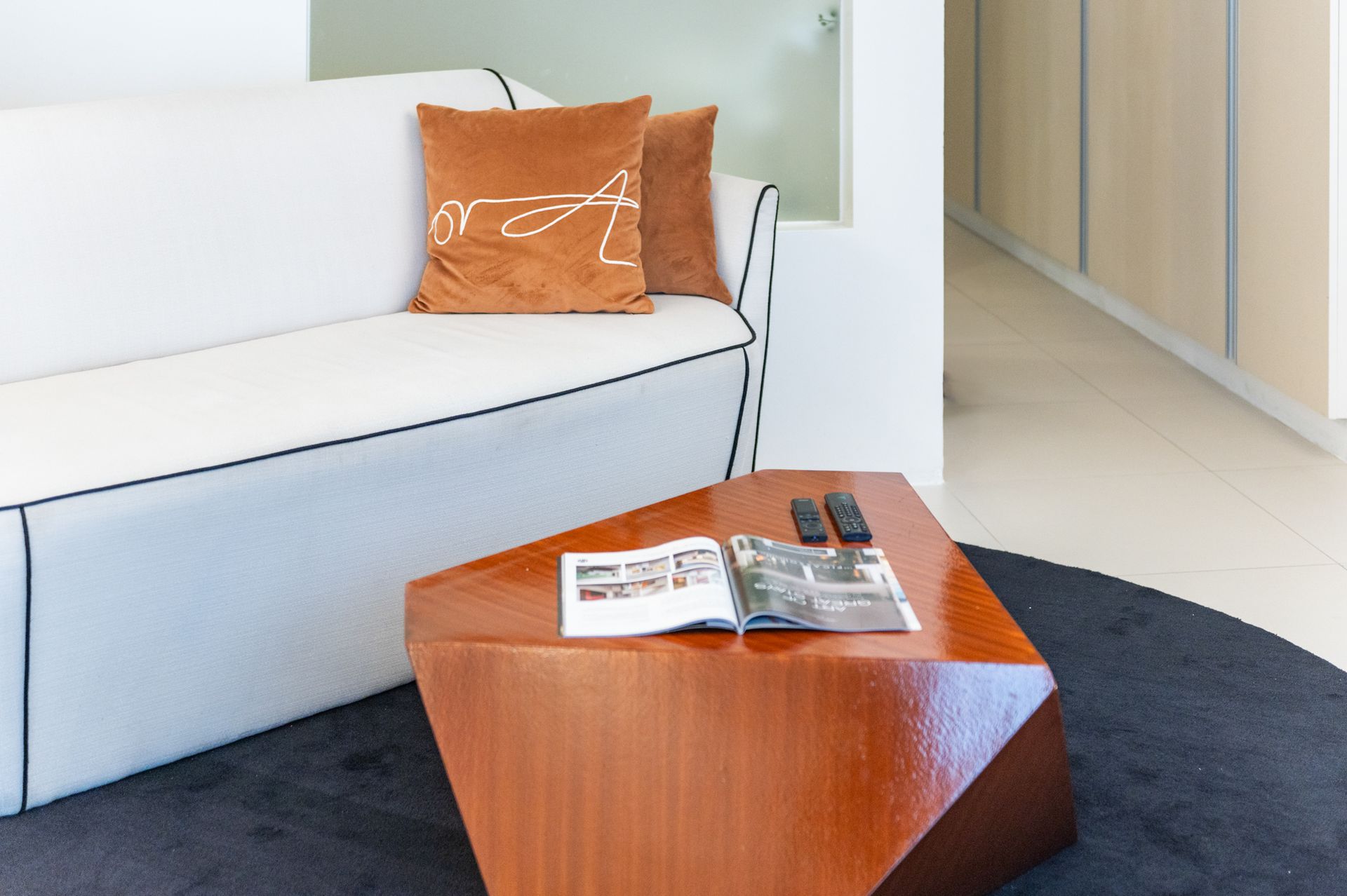 Modern living room with white sofa, orange cushion, and angular wooden coffee table with magazines.