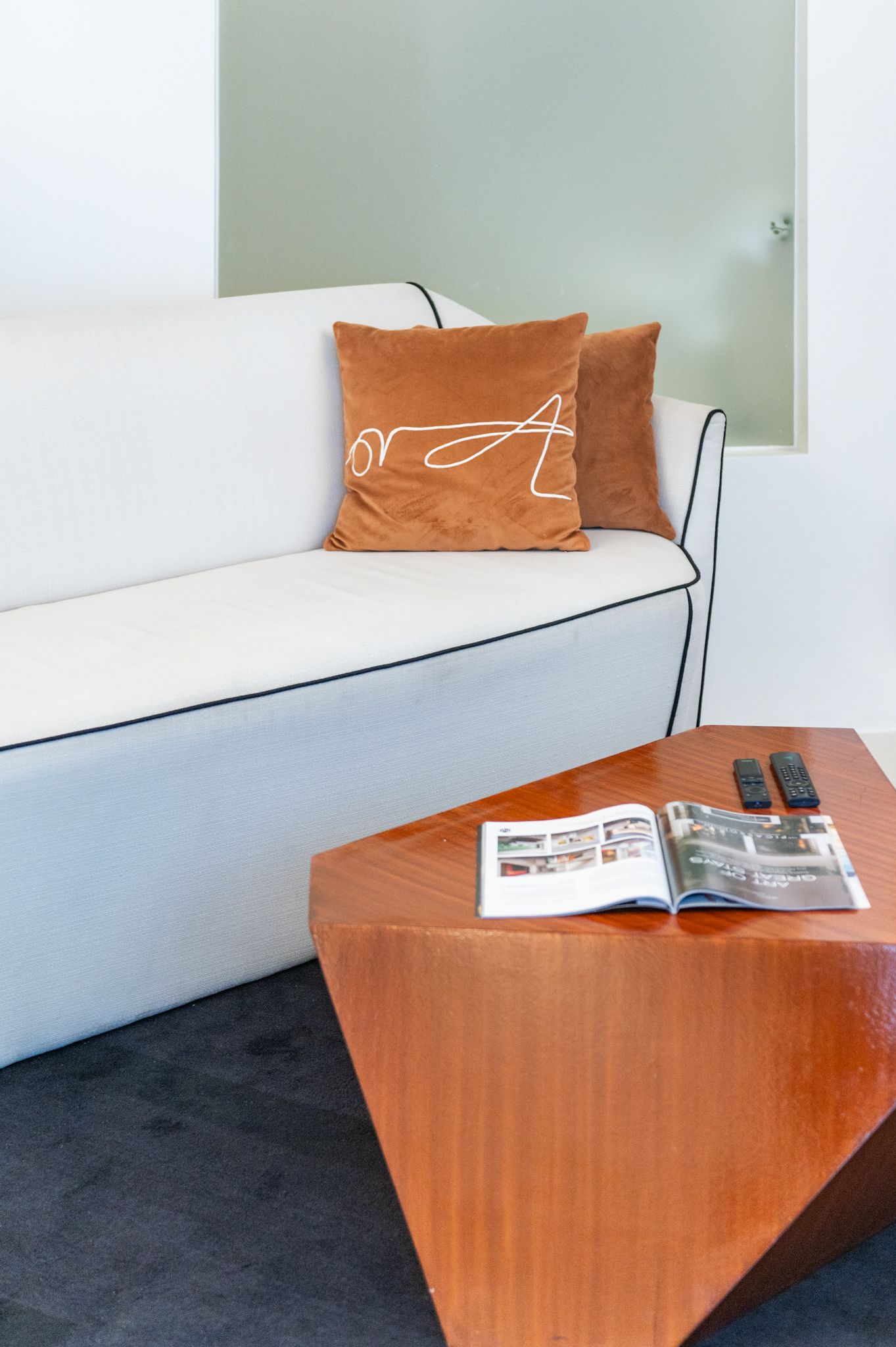 White sofa with two orange pillows, next to a geometric wooden coffee table.