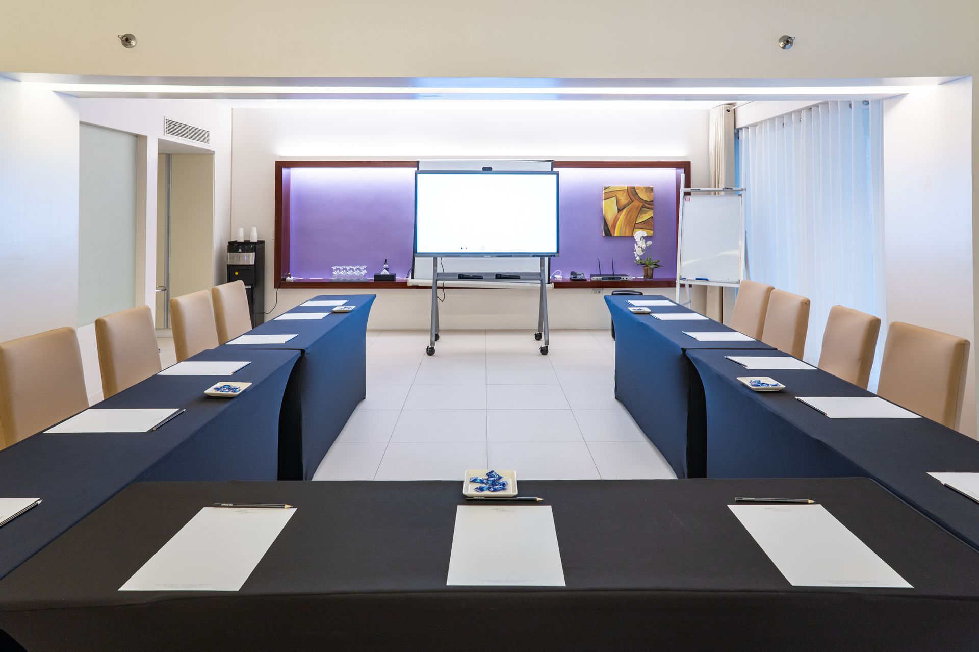 A conference room with tables and chairs and a projector screen