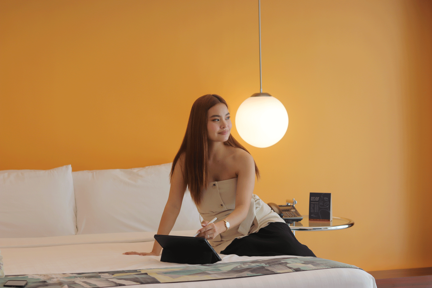 Woman sitting on a bed with a laptop in a bright orange bedroom