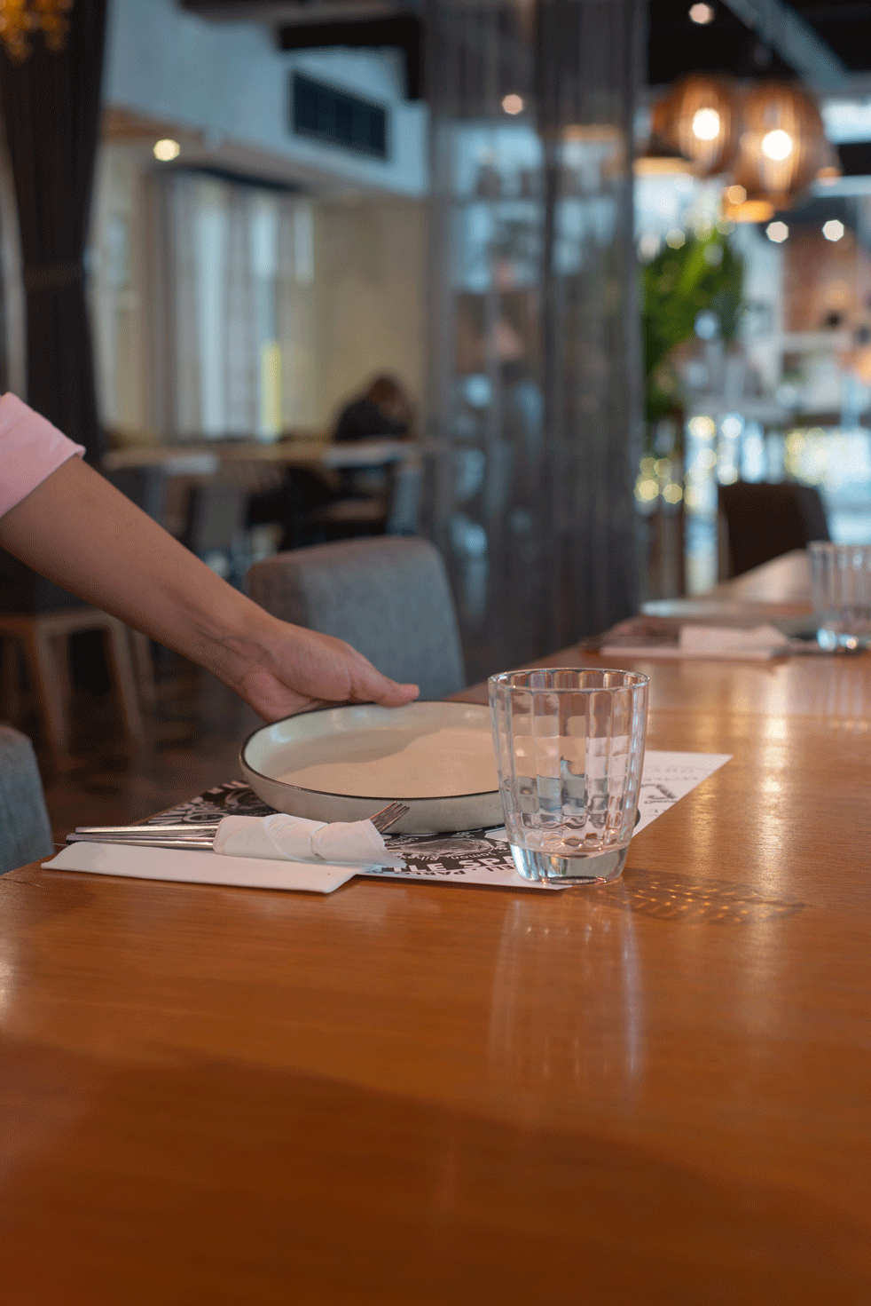 Waiter setting a place at a wooden dining table in a modern restaurant