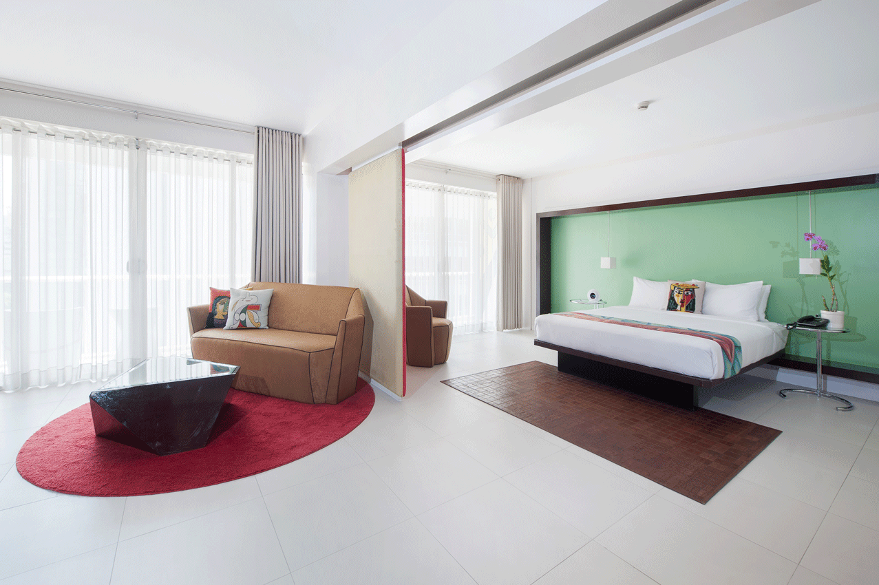 Bright modern bedroom with a large bed, lounge chair, red rug, and floor-to-ceiling curtains