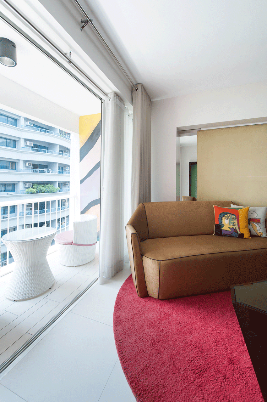 Bright living room with brown sofa, red rug, and balcony view at The Picass