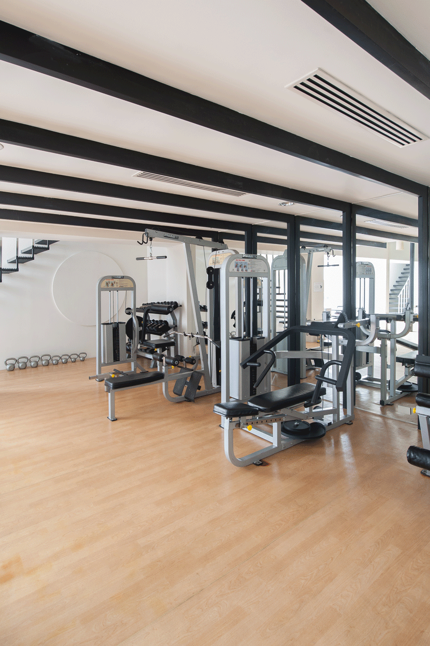Gym interior with various exercise machines, wooden floor, and a staircase.