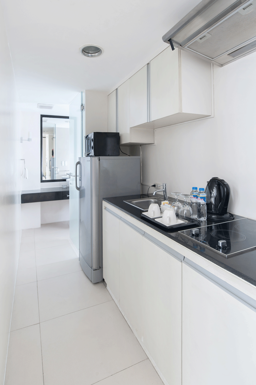 Small white kitchen with a refrigerator and countertop leading to a bathroom doorway.