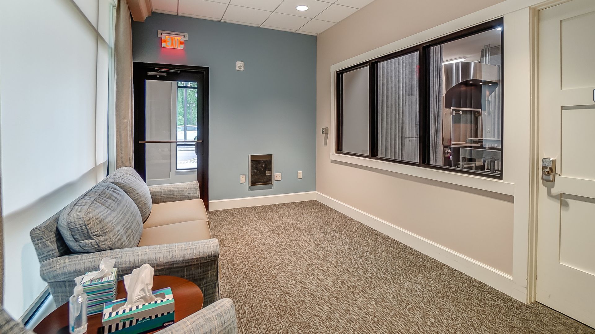 Private cremation witnessing room with seating area, with napkins on the side table, and an interior viewing window to the crematory equipment.