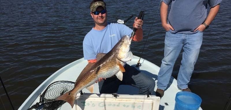 Two men are standing on a boat holding a large fish.