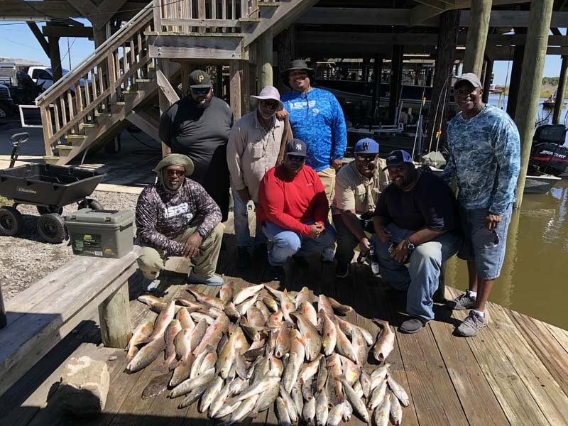 A group of men are posing for a picture with a pile of fish on a dock.